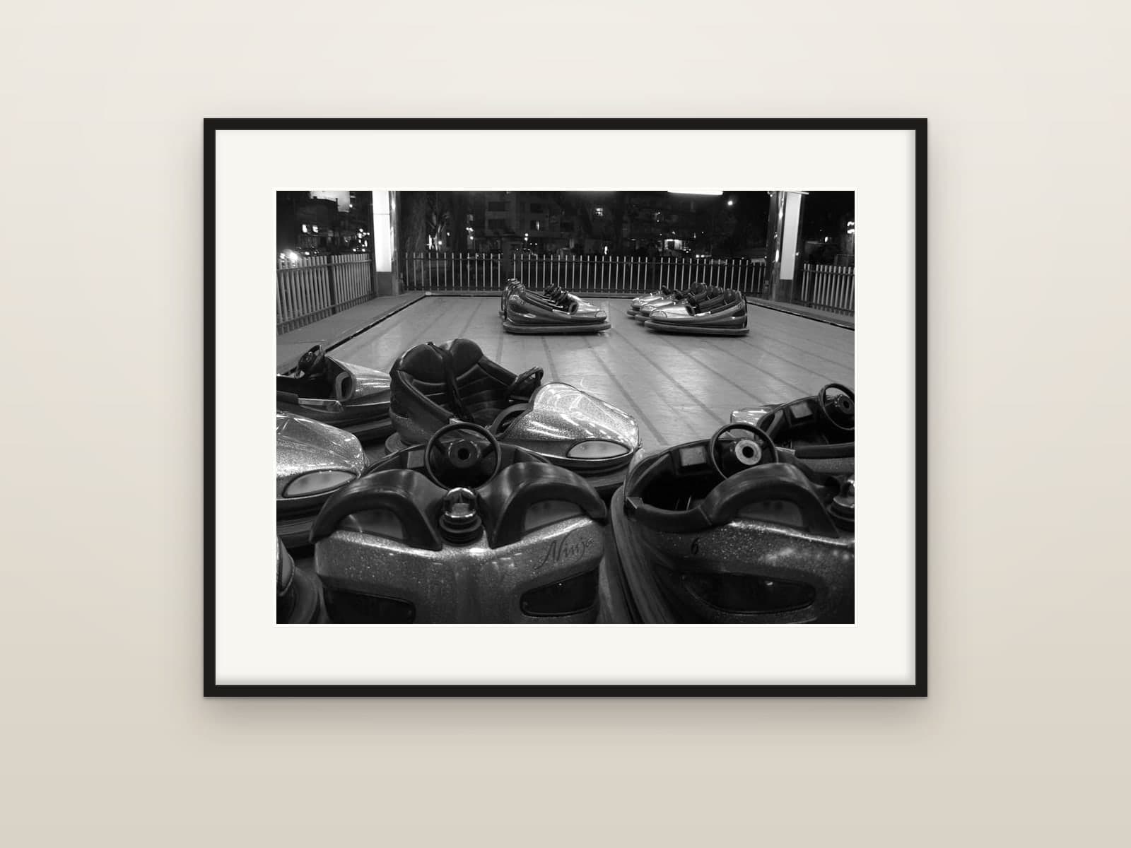 Empty bumper cars resting on the track of a fairground at night, shown as a framed print