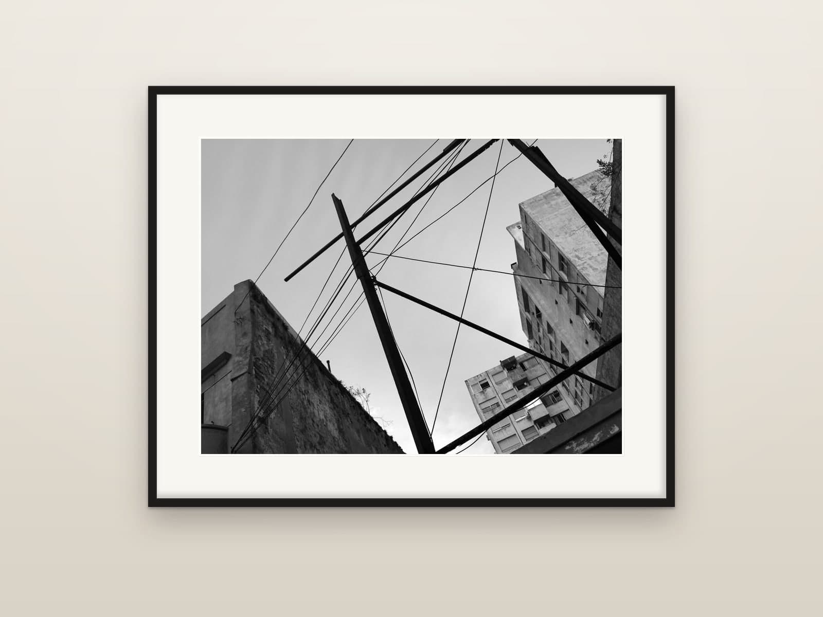 Utility poles and cables criss-crossing between old apartment buildings, shown as a framed print
