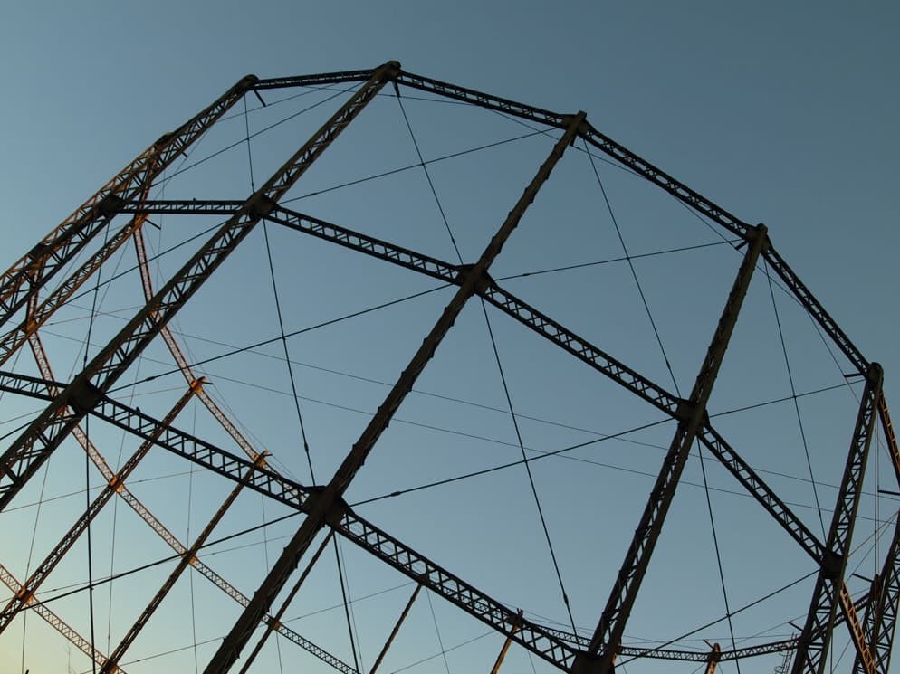 The iron lattice of a gasholder frame against a clear blue evening sky