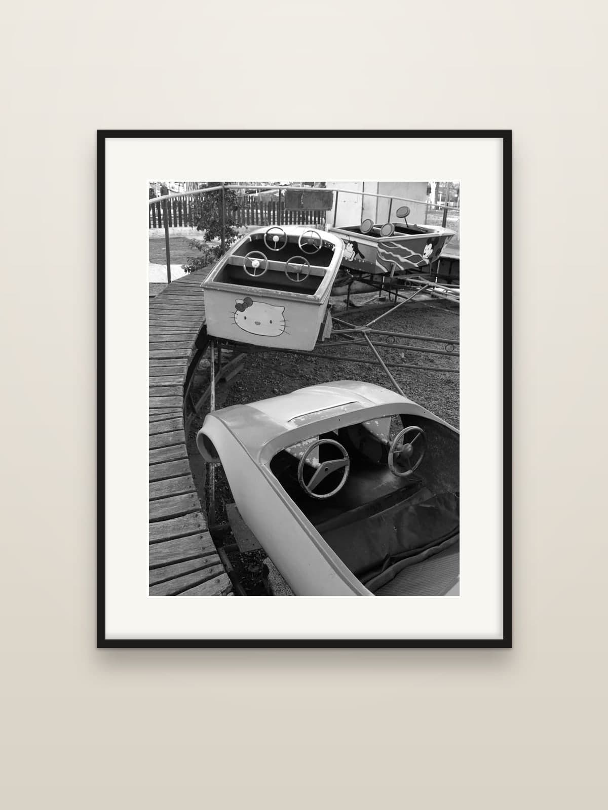 Small cars of a children's fairground ride, still and empty, shown as a framed print