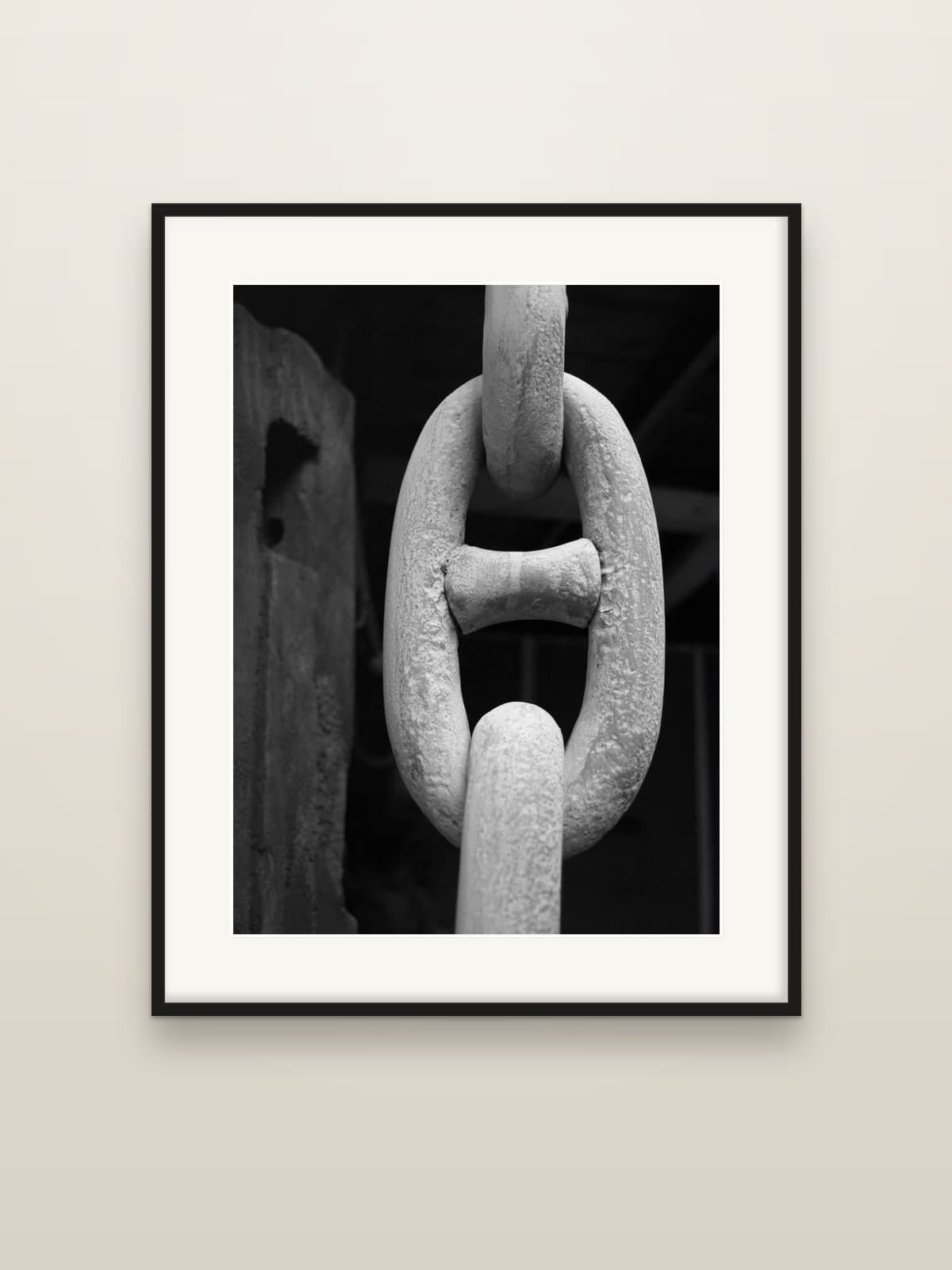 A heavy, weathered chain link hanging in a dark warehouse, shown as a framed print