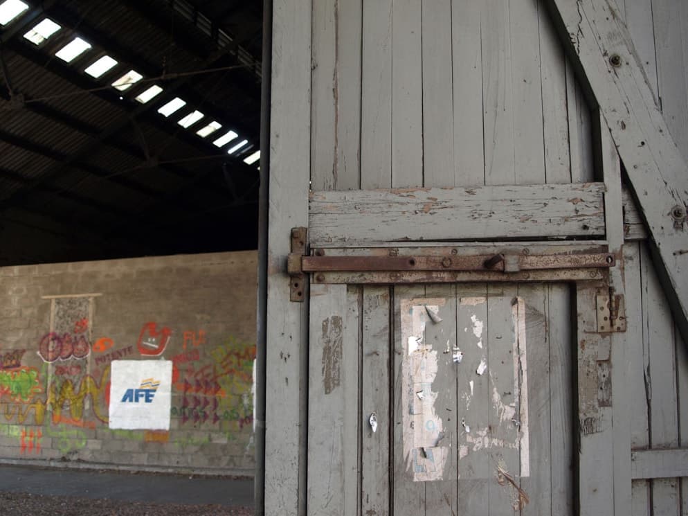 A worn wooden door with a rusted latch inside a railway shed with graffiti